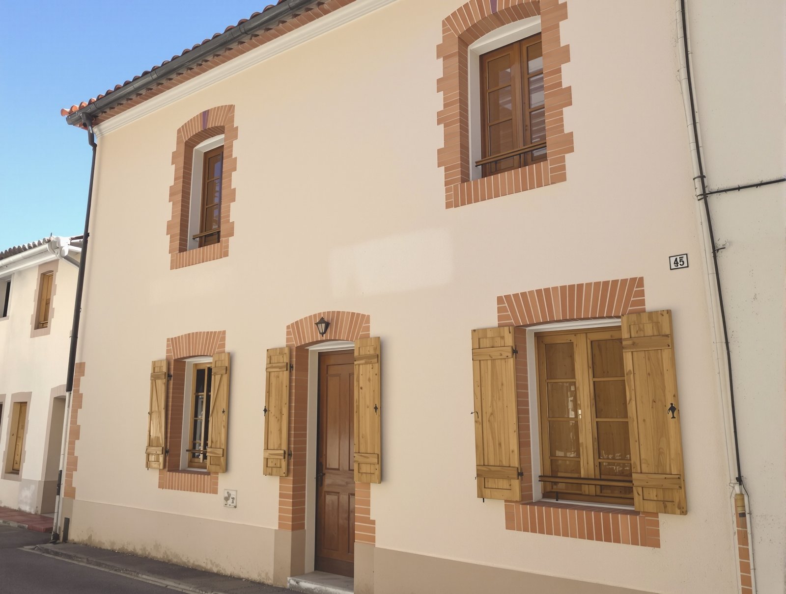 Façade de maison de village repeinte, enduit crème et encadrements de brique