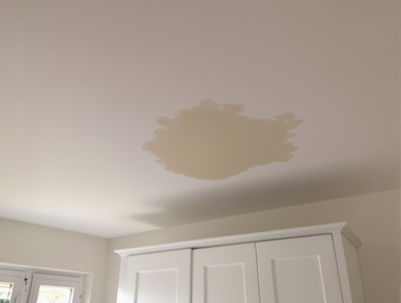 Auréole brune de dégât des eaux sur un plafond blanc de chambre, avant reprise en peinture